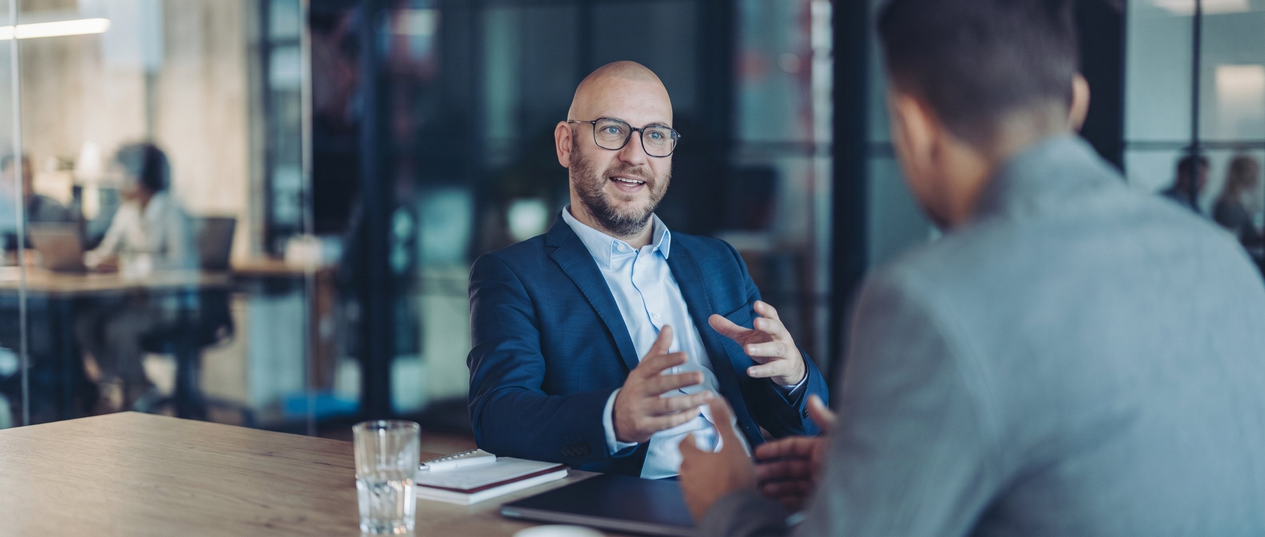 A consultant in a blue blazer talking with a client across a table in a modern office